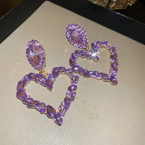 Close-up of sparkling purple heart-shaped earrings with gold metal and starburst effects