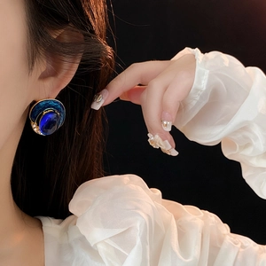 Close-up of vintage royal style gold earrings with blue enamel and gemstones on model