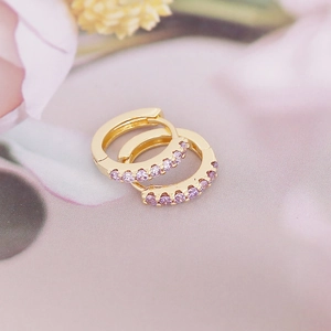Macro shot of gold-plated hoop earrings with purple zircon stones on pink background