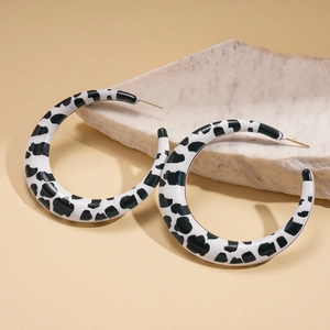 Detailed macro view of C-shaped acrylic earrings featuring black and white cow print patterns