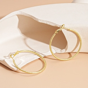 Detail of gold geometric hoop earrings with matte finish on minimalist stone display