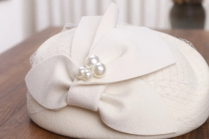 Close-up of white wool beret featuring elegant mesh veil and bow with pearl accents