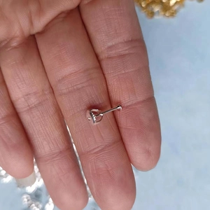 Macro shot of a silver screw-back earring post held between fingers for size reference