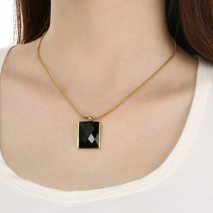 Gold snake chain necklace with rectangular black glass pendant worn by a model