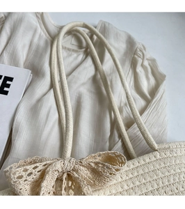Close-up of a cream woven tote bag featuring a delicate lace bow and sturdy shoulder straps