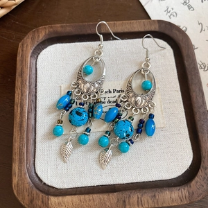 Detailed close-up of retro bohemian earrings with turquoise beads and leaf tassels on a tray