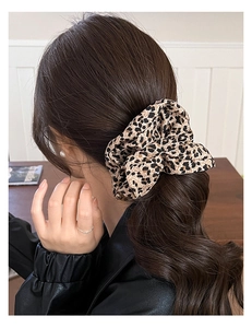 Detail view of leopard print hair scrunchie worn on a high ponytail by a model