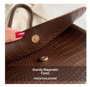 Detail of crocodile-textured brown tote bag showing the secure golden magnetic closure