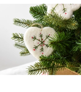 Close-up of white wool felt heart ornament with green snowflake embroidery and jute string
