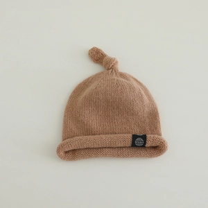 Détail du bonnet tricoté marron clair pour bébé avec nœud et écusson logo