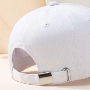 White cotton baseball cap with adjustable metal buckle strap on a warm minimalist background