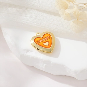 Detail of a golden heart locket with orange enamel and SWEET text on white marble