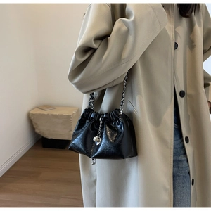 Detail of black pleated cloud bag with pearl chain accessory on beige trench coat