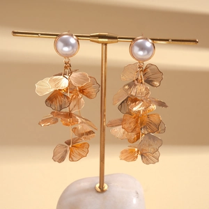 Detailed view of gold ginkgo leaf drop earrings with pearls on a T-bar display stand