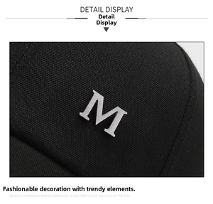 Close-up of black cotton twill fabric texture and silver metal M letter on baseball cap