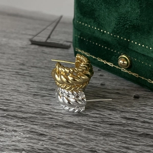 Close-up of gold and silver twisted C-shaped earrings next to a velvet gift box