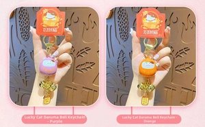Close-up of Maneki Neko Daruma bells in purple and orange with golden keyrings