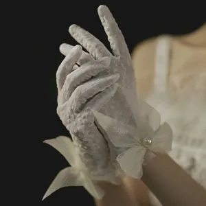 Close-up of white lace bridal glove with a satin bow and central pearl accent detail