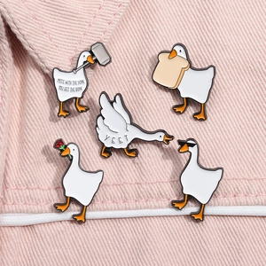 Detail of five cute white swan enamel pins with internet meme text on pink denim fabric