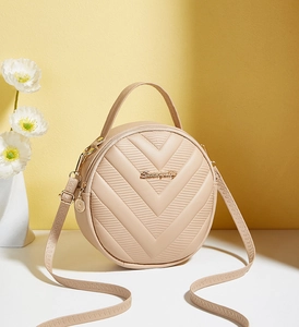 Detailed view of beige circular handbag with V-shaped quilting and gold metal logo