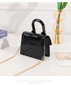 Detail of black glossy jelly bag with golden chain strap on a white table surface