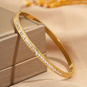 Macro shot of gold stainless steel bangle with square zircon inlay on champagne jewelry box