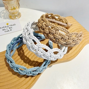 Three braided leather headbands in blue, white, and beige on a wooden display board