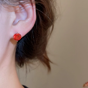 Macro side view of silver stud earrings featuring a brilliant red zircon in 4-prong setting