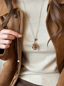Détail d'un long collier argenté avec pendentif marron et perle porté sur un pull