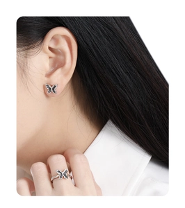 Detail view of a black butterfly stud earring and ring set on model's hand and ear