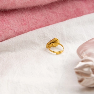 Detailed side view of golden heart ring with adjustable open band on soft pink silk
