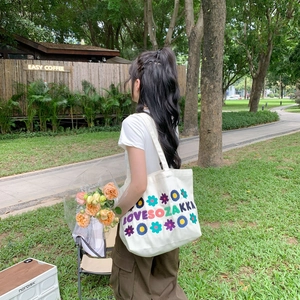 Detail of floral embroidery on a cream canvas tote bag worn by a model in a park