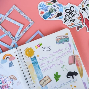 DIY scrapbook set showing stickers and decorative frames on a pink spiral journal