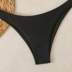 Detail of high-cut black bikini bottoms on a woven beach mat with a sun hat accessory