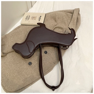 Detailed close-up of dark brown dog-shaped shoulder bag on beige fabric with a book