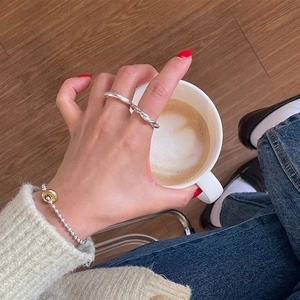 Close-up of a silver twisted rope ring and beaded bracelet styled with a coffee cup