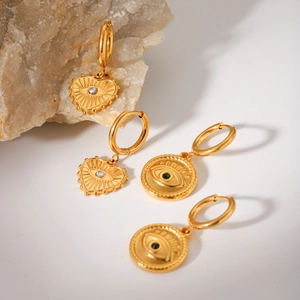Detailed macro view of gold evil eye heart and round earrings on a natural stone base