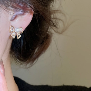 Close-up of elegant bow earrings with pearl and shimmering zircon stones on ear