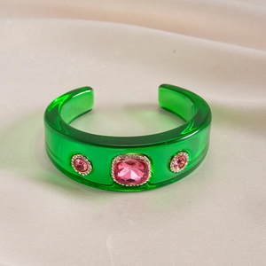 Detailed macro view of green resin cuff bangle with pink gemstones and gold-tone crystals
