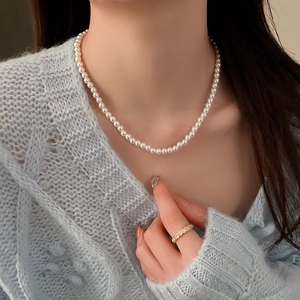 Gros plan d'un collier de perles blanches vintage porté par un mannequin en pull bleu