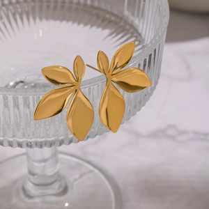 Close-up of golden clover earrings hanging on a textured glass rim over white marble