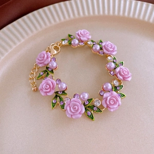 Detail of flower bracelet with pink resin roses and purple pearls on golden chain