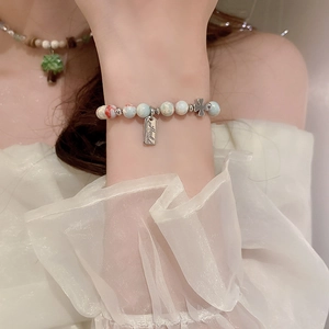 Detail of beaded bracelet with light blue marble beads and silver cross charm