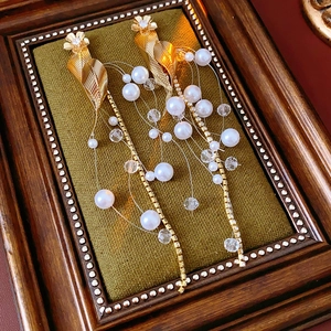 Detail of golden leaf earrings with pearl and bead tassels on a vintage wooden frame