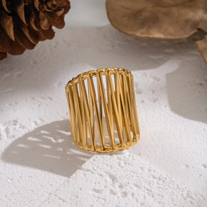 Artistic golden hollow-out wide band ring displayed on white stone with dry leaves