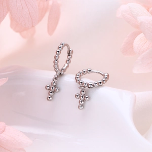 Detail of silver S925 cross earrings with bead charms on a white ceramic display
