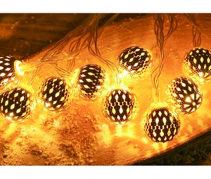 Macro shot of warm LED light shining through intricate hollow metal balls on dark wood