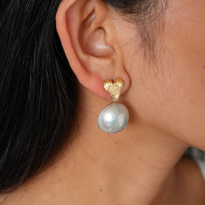 Detail of heart-shaped gold earring with brushed texture and grey pearl on model