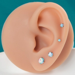 Detail view of four different sizes of round opal stud earrings on a silicone ear model