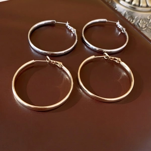 Eleganti orecchini a cerchio a tubo vuoto placcati oro e argento su sfondo di pelle